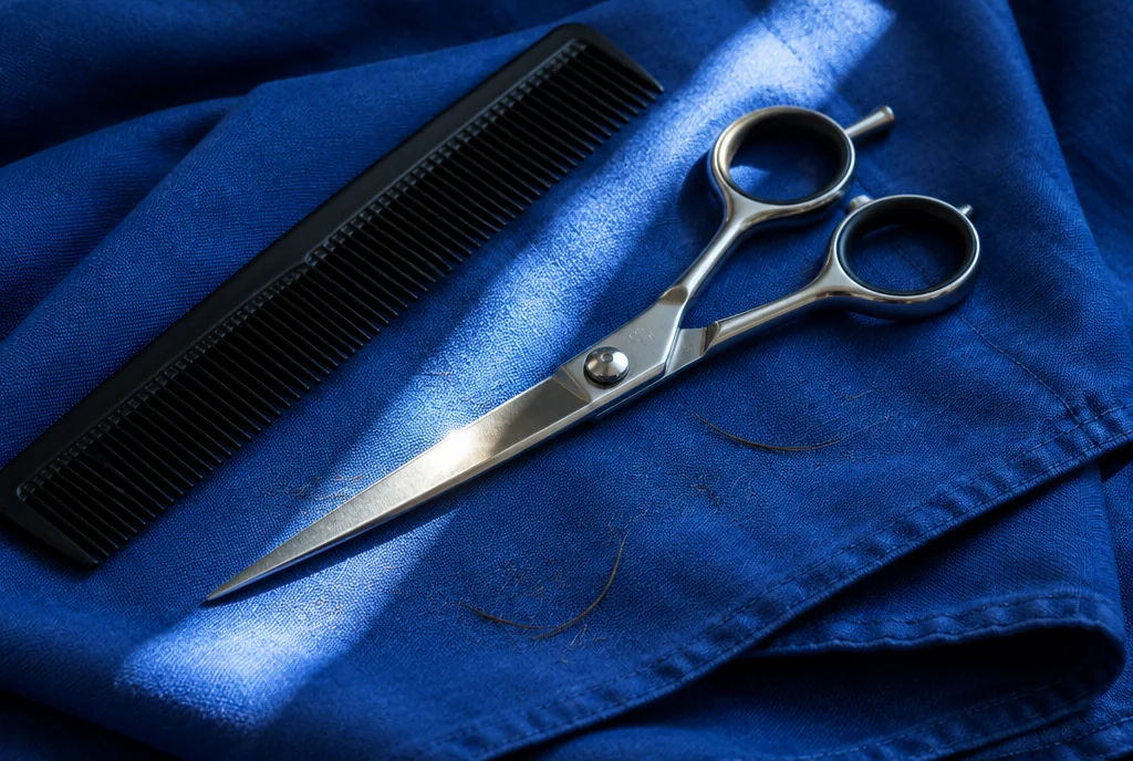 Barber scissors and a comb on a folded blue cape, in a strip of sunlight.